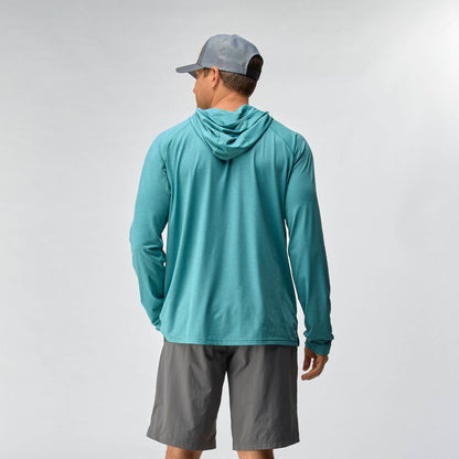 A man wearing the NRS Silkweight Hoodie - Men's in teal, paired with gray shorts and a gray cap, stands facing away against a plain light background.