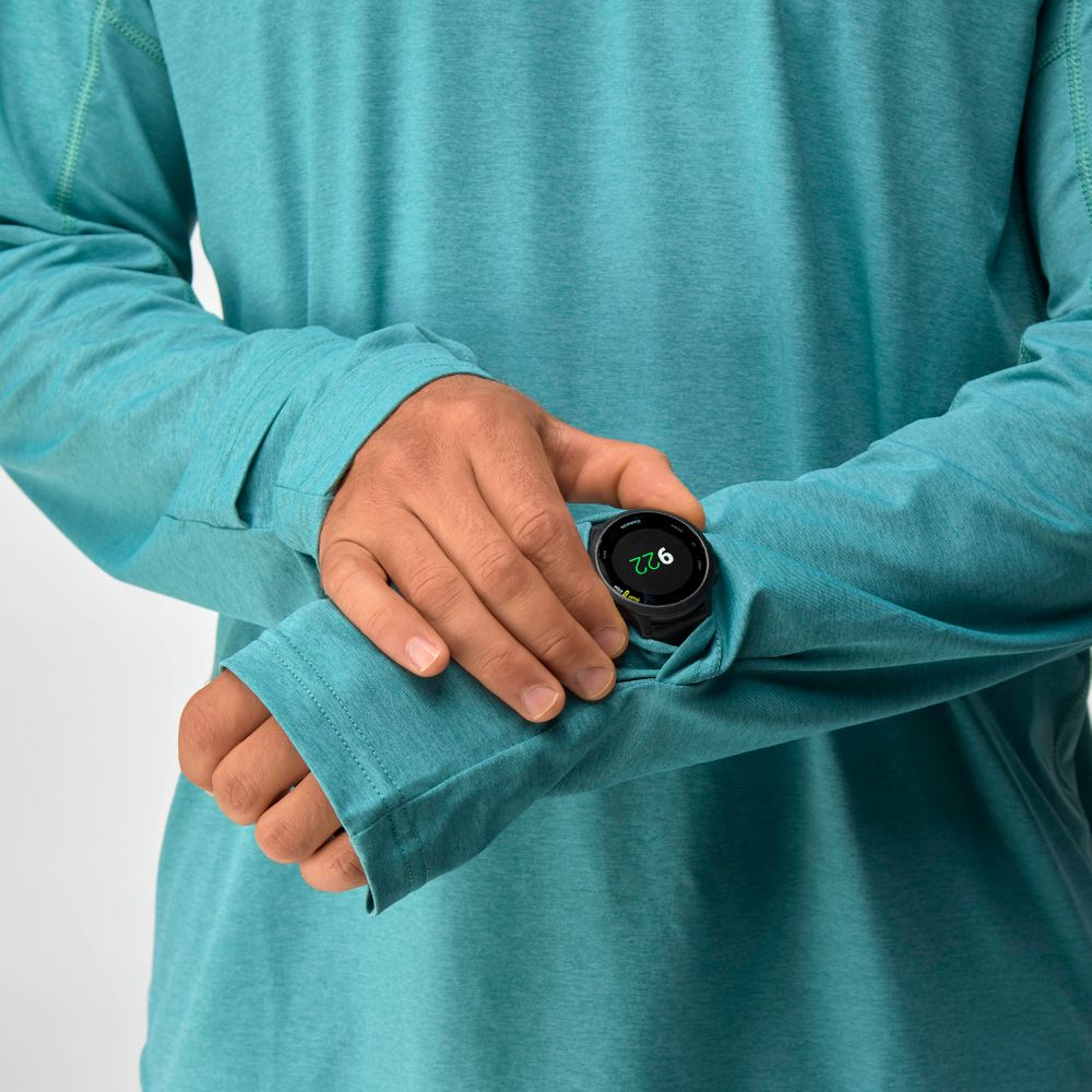 A man in an NRS Silkweight Hoodie (teal, moisture-wicking) adjusts the cuff, revealing a black smartwatch showing 2:26.