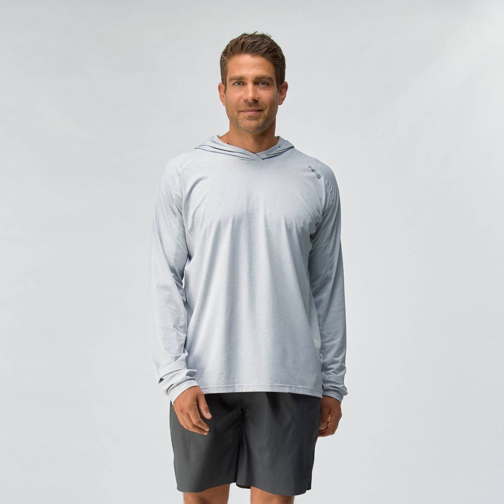 A man stands against a plain background wearing the NRS Silkweight Hoodie - Men's in light gray for sun protection and dark shorts, looking at the camera with a neutral expression.