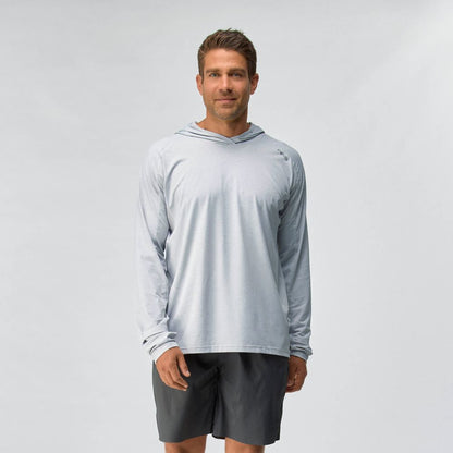 A man stands against a plain background wearing the NRS Silkweight Hoodie - Men's in light gray for sun protection and dark shorts, looking at the camera with a neutral expression.
