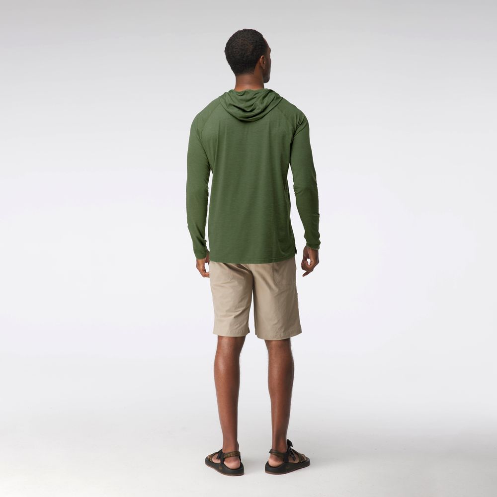 A man faces away, wearing the NRS Silkweight Hoodie - Men's in green for sun protection, along with beige shorts and black sandals, against a plain white background.