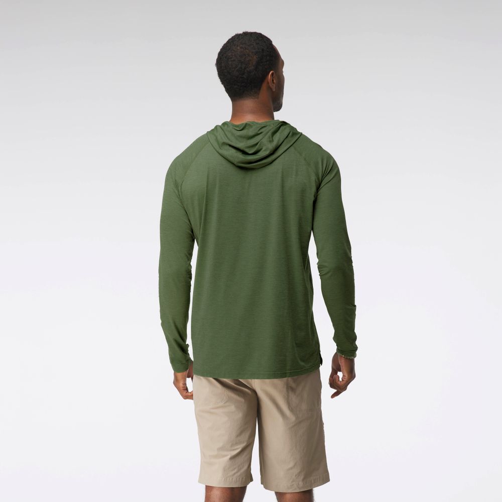 A man in the NRS Silkweight Hoodie - Men's stands facing away in a green top and beige shorts against a plain light background, showcasing sun protection and moisture-wicking comfort.