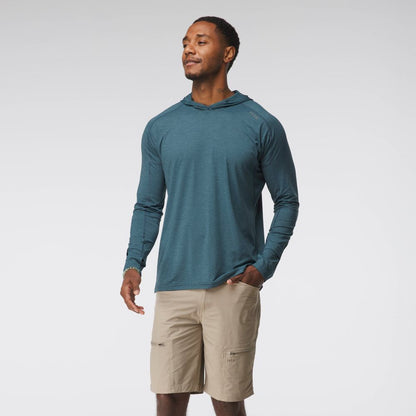 A man stands against a plain background wearing the NRS Silkweight Hoodie - Men's in teal and beige shorts, looking to the side with one hand in his pocket.