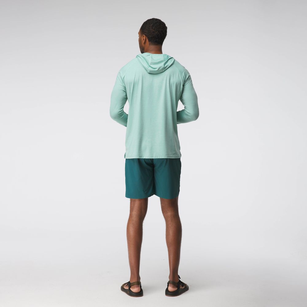 A man stands facing away, wearing the NRS Silkweight Hoodie - Men's in light green, paired with teal shorts and black sandals against a plain white background.