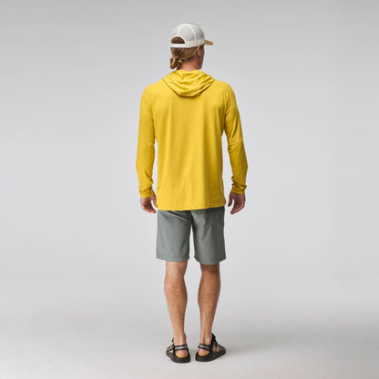 A man faces away, wearing the NRS Silkweight Hoodie - Men's in yellow for sun protection, paired with gray shorts, black sandals, and a white cap against a plain gray background.