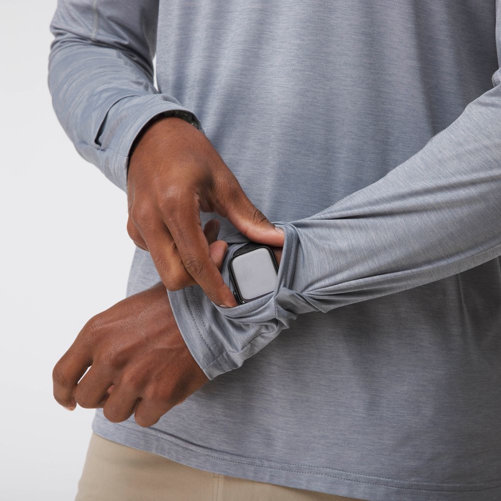 A person slips a smartwatch into a hidden sleeve pocket on the NRS Silkweight Hoodie - Men's, a light gray top designed for moisture wicking and sun protection.