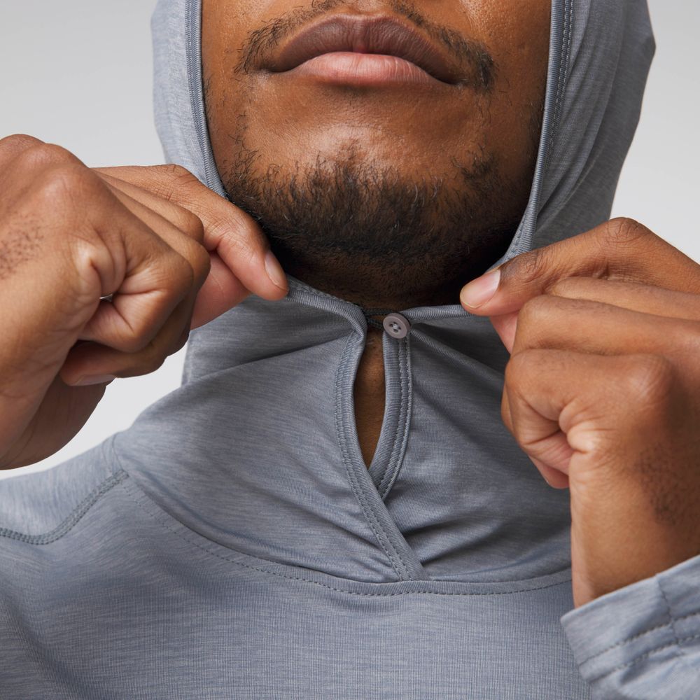 Close-up of a man pulling up the hood of the NRS Silkweight Hoodie - Men's in light gray, securing it at the neck with a small button for enhanced sun protection.
