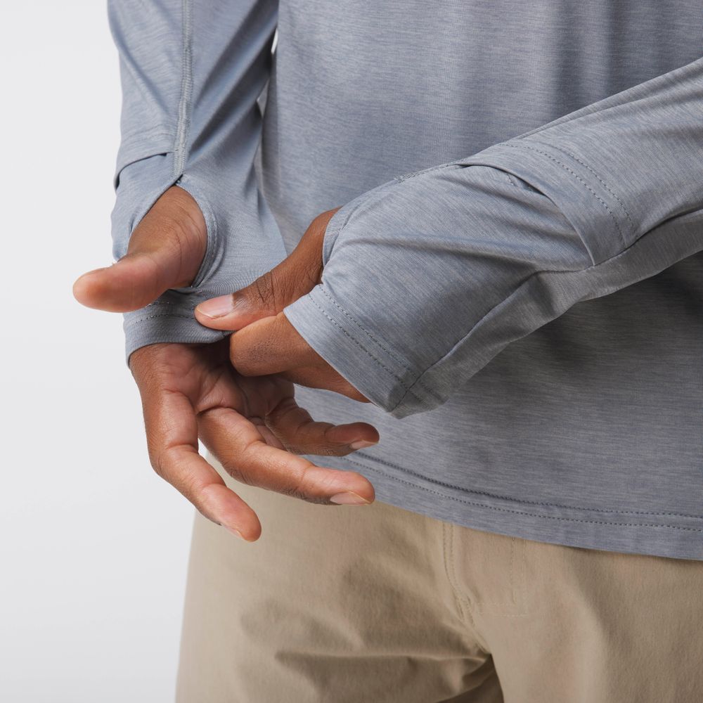 A man wearing the NRS Silkweight Hoodie in light gray adjusts its sleeve with thumbholes over his hand, paired with beige pants.