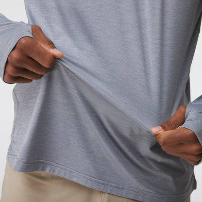 A person stretches the hem of the NRS Silkweight Hoodie - Men's, a light gray, moisture-wicking long-sleeve shirt, showcasing its flexibility; only their torso and hands are visible.