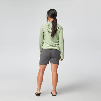 A woman faces away from the camera wearing the NRS Silkweight Hoodie - Women's for sun protection, paired with gray shorts and black sandals, against a plain light gray background.