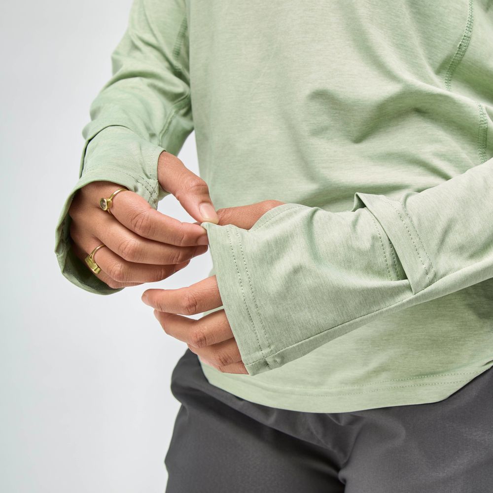 Woman wearing the NRS Silkweight Hoodie - Women's in light green, adjusting the sleeve to show off gold rings—an ideal sun-protective base layer featuring thumb holes.