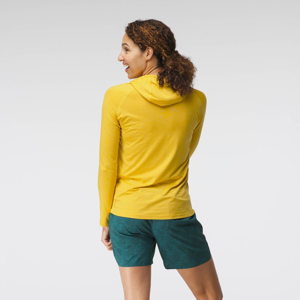 A woman wears the NRS Silkweight Hoodie and teal patterned shorts, standing and glancing over her left shoulder against a plain background—perfect as sun protection or a women’s base layer.