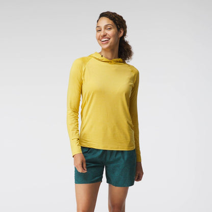 A woman wearing an NRS yellow Silkweight Hoodie paired with green shorts smiles against a plain white background.