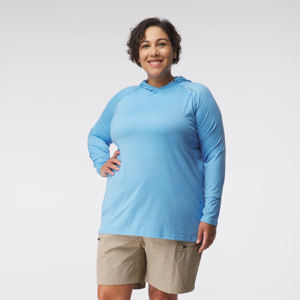 A woman faces the camera, smiling, in the NRS Silkweight Hoodie - Women's (light blue) with tan shorts, posed against a plain white background.