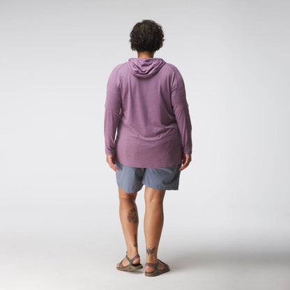 A person faces away, wearing the NRS Silkweight Hoodie - Women's in purple for sun protection, paired with gray shorts and sandals, showing lower leg tattoos against a plain white background.