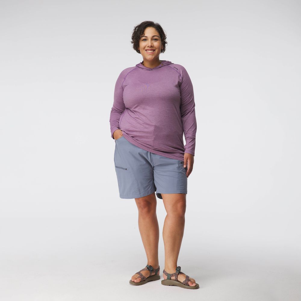 A woman stands facing forward against a white background, wearing the NRS Silkweight Hoodie - Women's (a long-sleeved purple sun protection top), light blue shorts, and sandals.