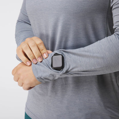 A woman in an NRS Silkweight Hoodie, featuring technical sun-protective fabric, displays a smartwatch through a thoughtful sleeve window.