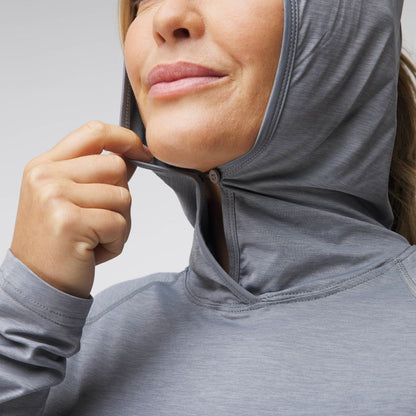 A person in the light gray NRS Silkweight Hoodie - Women's, crafted from technical fabrics for comfort, grips the zipper near their chin. This versatile top is designed for sun protection, ideal for outdoor adventures and everyday use.