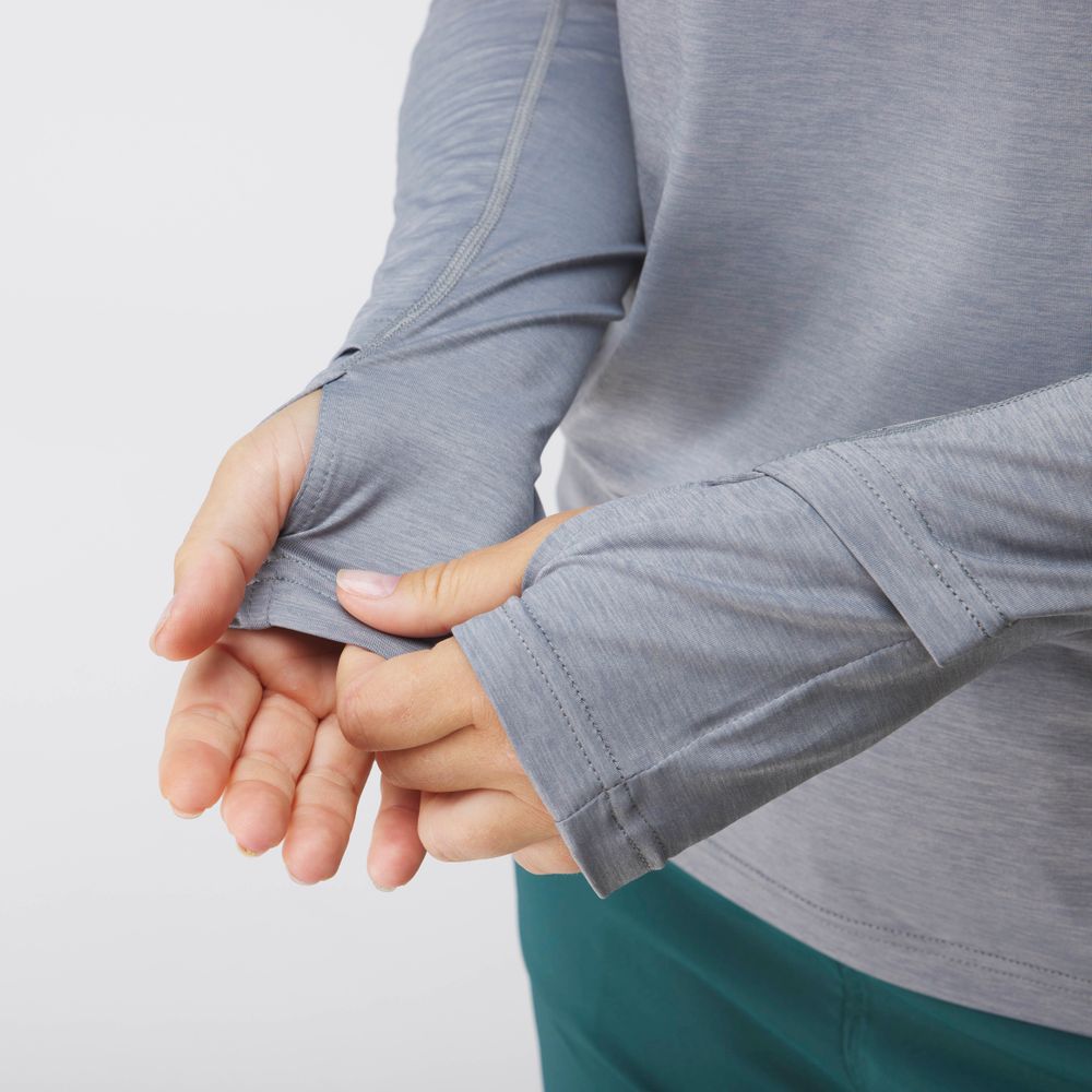 A person wears the NRS Silkweight Hoodie - Women's in light gray, highlighting the thumbhole feature on one sleeve.