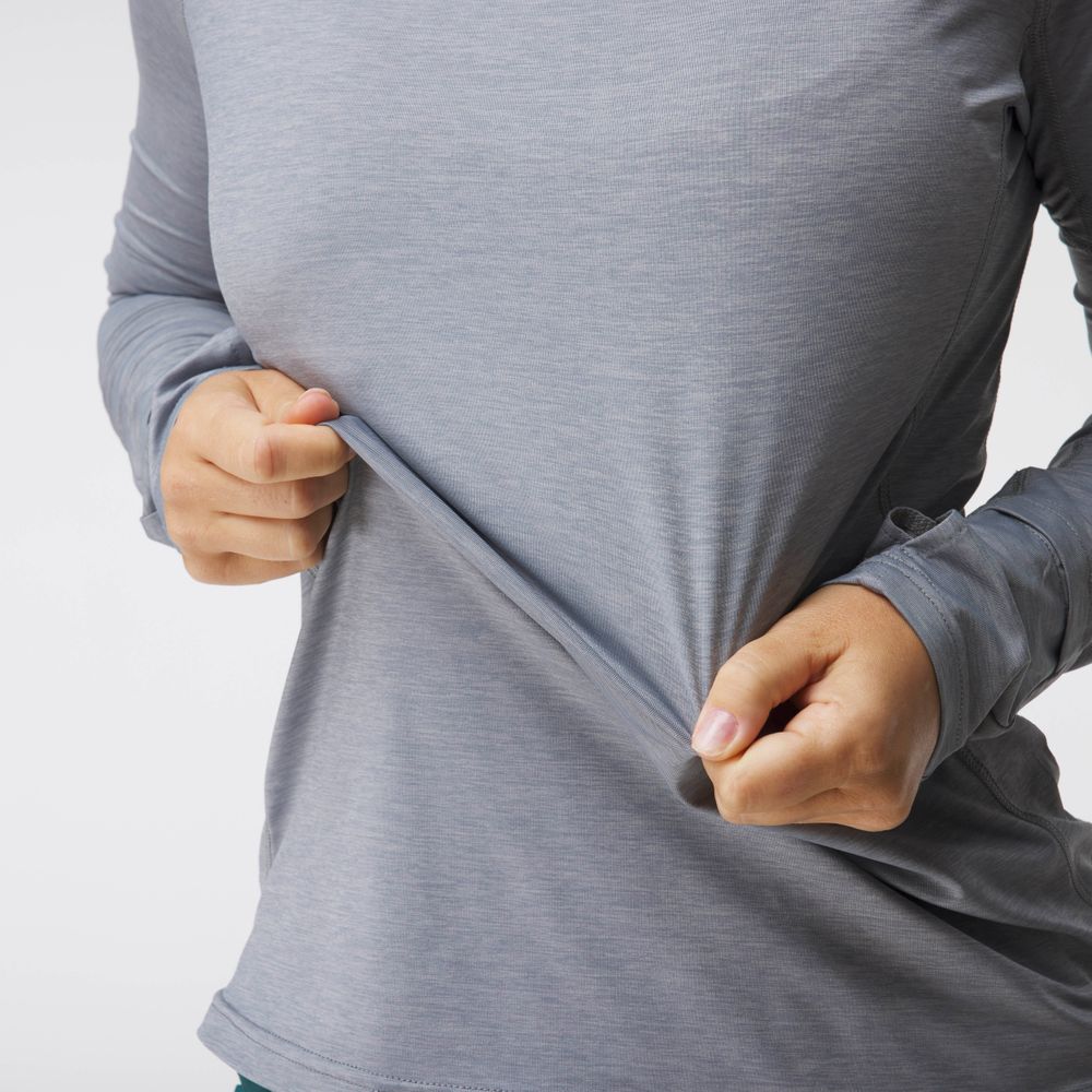 A woman wearing the NRS Silkweight Hoodie - Women's stretches the long-sleeved gray fabric outward with both hands.