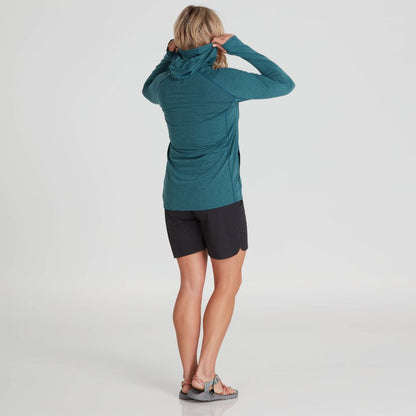 A person with long blonde hair is facing away, wearing the NRS Silkweight Vesi Hoodie - Women's in teal with UPF 50+ sun protection, black shorts, and sandals against a plain white background.