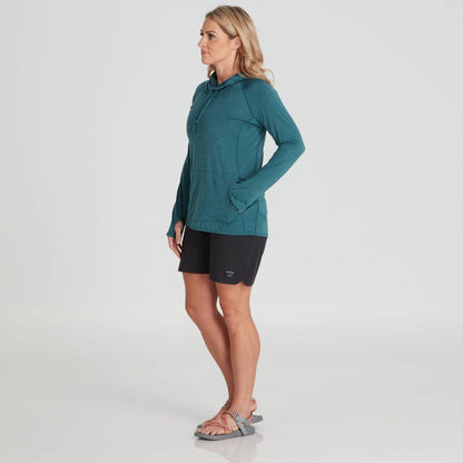 A person stands in a turquoise Silkweight Vesi Hoodie by NRS, featuring UPF 50+ sun protection, paired with black shorts. Hands in pockets, wearing sandals against a plain white background, highlighting the breathable attire for sunny adventures.