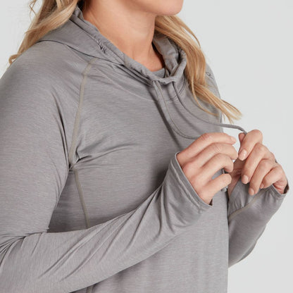 Wearing the NRS Silkweight Vesi Hoodie - Women's in light gray, made from recycled material, one adjusts the hood's drawstring. This versatile long-sleeve top offers UPF 50+ sun protection for comfort and safety in the sun.