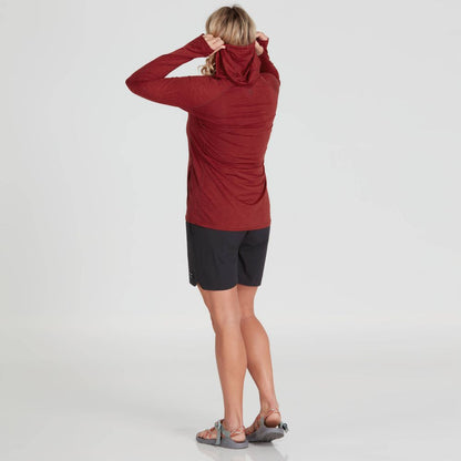 A person is adjusting the hood of a red NRS Silkweight Vesi Hoodie with UPF 50+ while wearing black shorts and sandals, facing away against a plain background.
