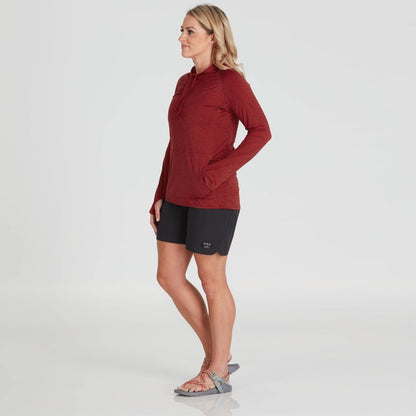 A woman in a red NRS Silkweight Vesi Hoodie with UPF 50+ stands against a plain background, wearing black shorts and sandals, facing slightly to the right.