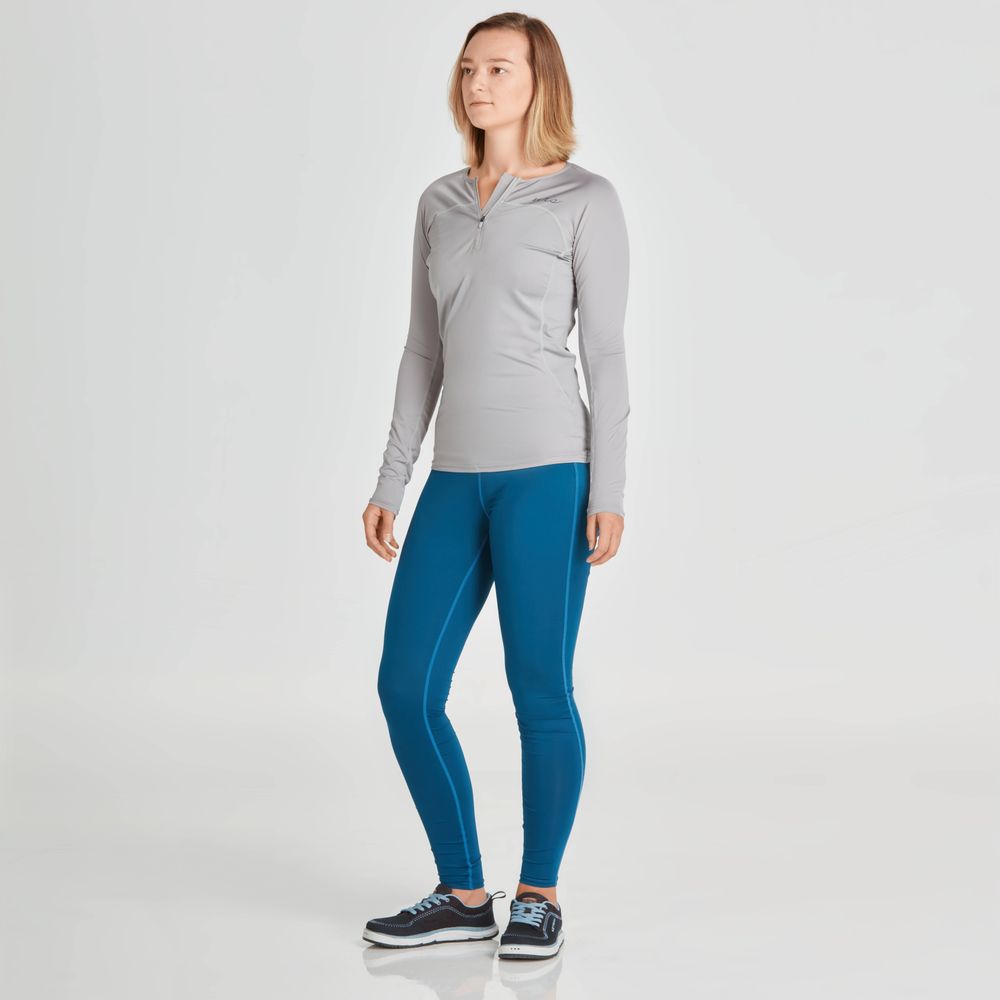 A person wearing Ava Rashguard Pants - Women's by NRS, featuring a gray long-sleeve swim tight and blue leggings crafted from recycled fabric, stands against a plain background.