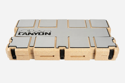Rectangular cork and metal case with black latches and "Canyon Coolers" logo on the lid, featuring an EVA foam liner, contains Cooler Traction Pads; shown closed against a white background.