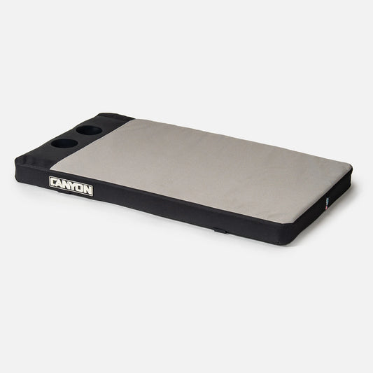 The Cooler Seat Pad by Canyon Coolers is a gray and black rectangular padded mat with waterproof canvas, two silicone cup holders, and a "Canyon" logo on the side.