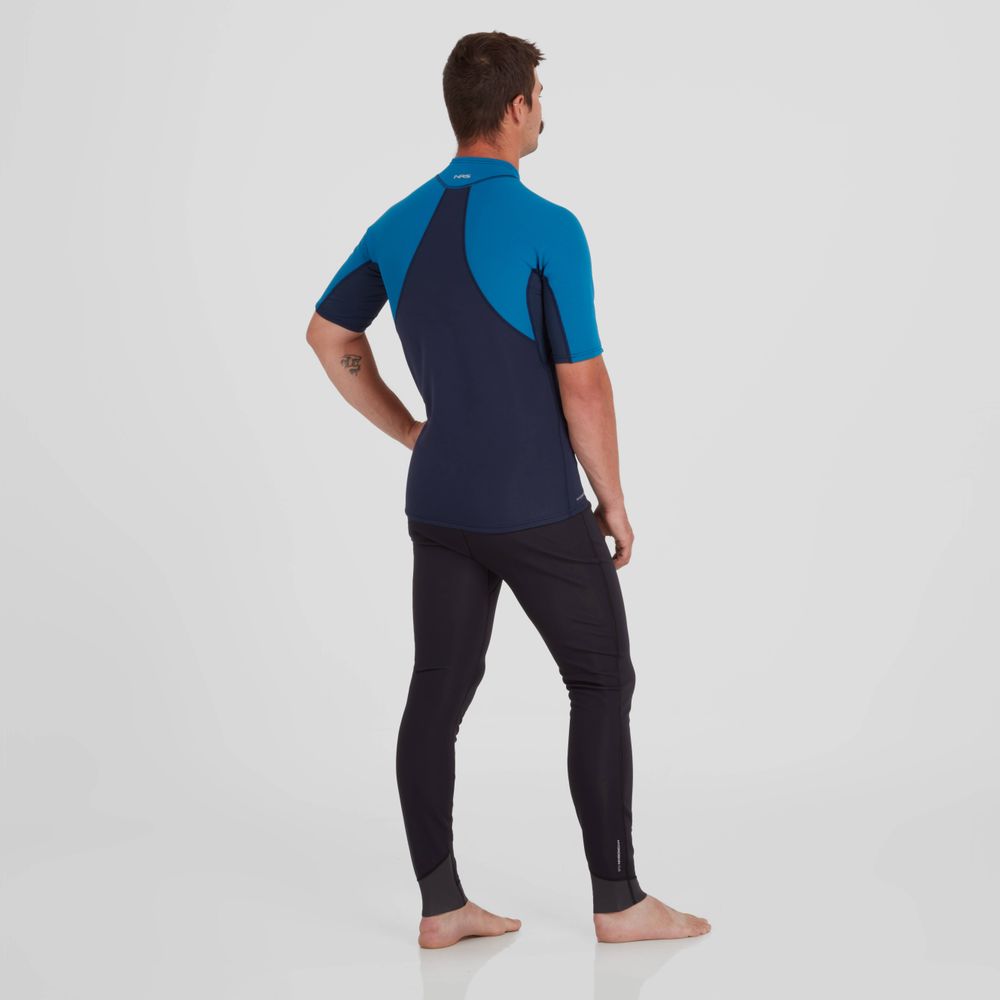 A man wearing the Hydroskin 0.5mm Short Sleeve Shirt by NRS, in blue and black, stands barefoot on a plain background, highlighting its exceptional paddling performance benefits.