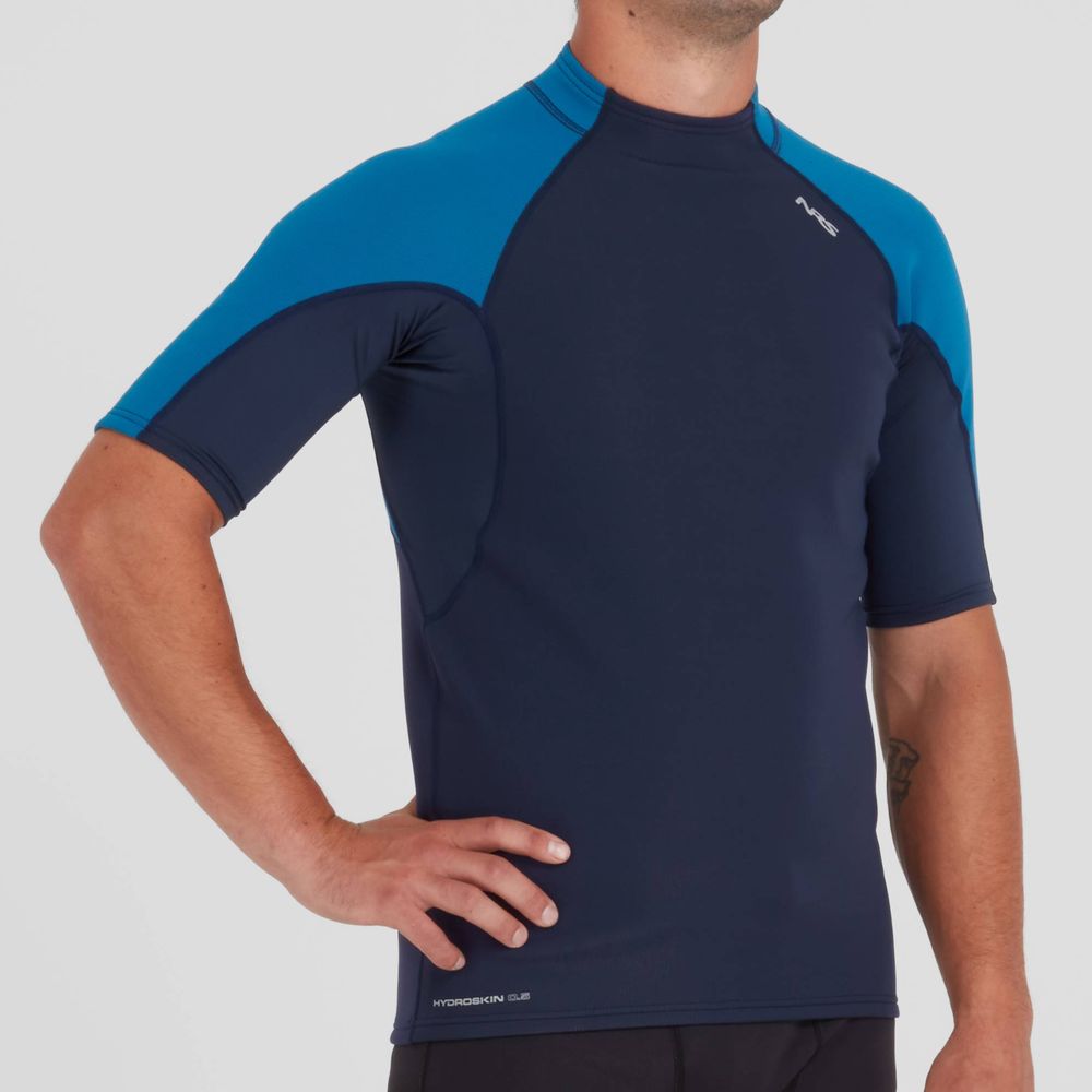 A man donning a NRS Hydroskin 0.5 Short Sleeve Shirt - Men's, a blue and navy short sleeve shirt for water retention purposes.