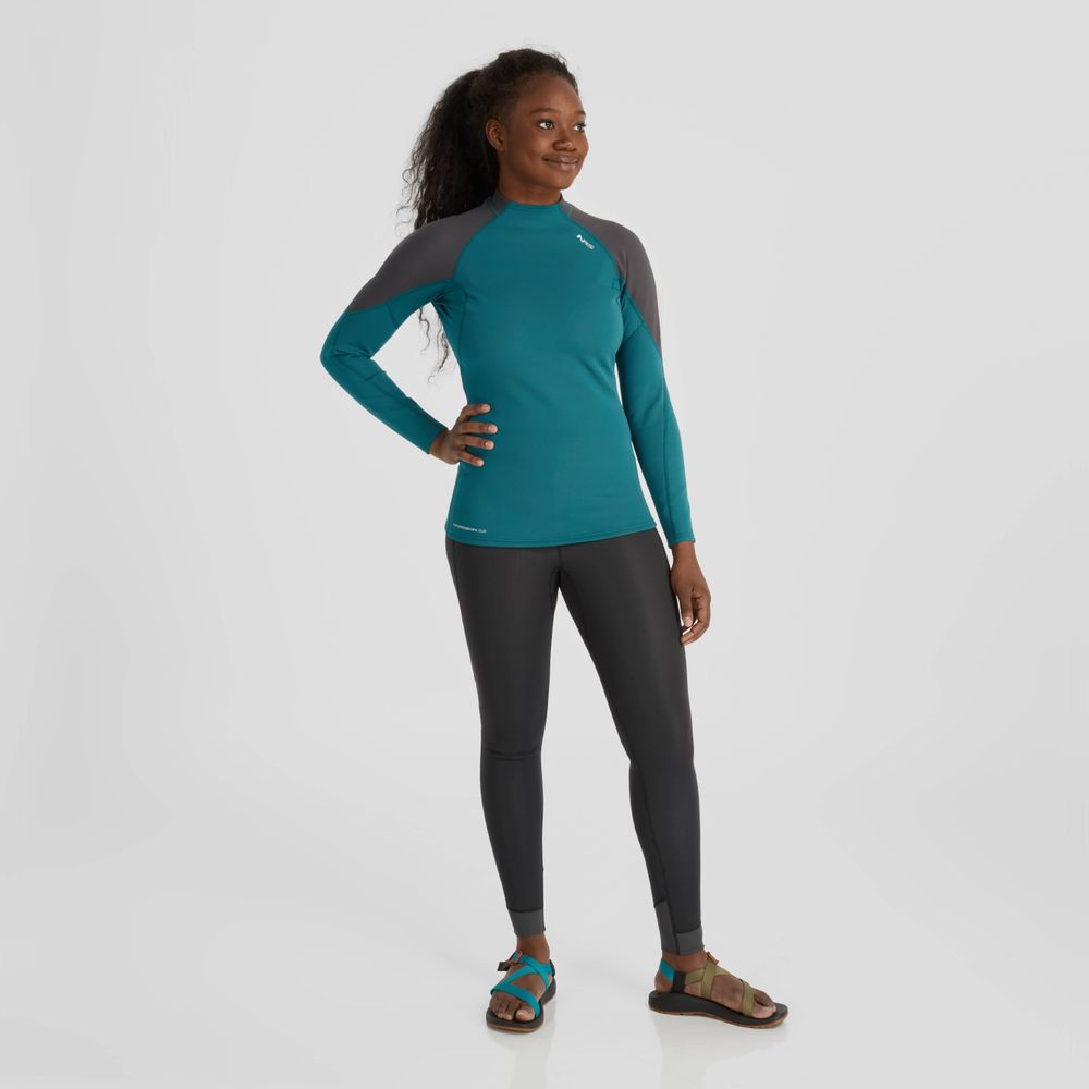 A person in an NRS Hydroskin 0.5mm Long Sleeve Shirt for women and sandals stands against a white background, ready for optimal paddling performance.