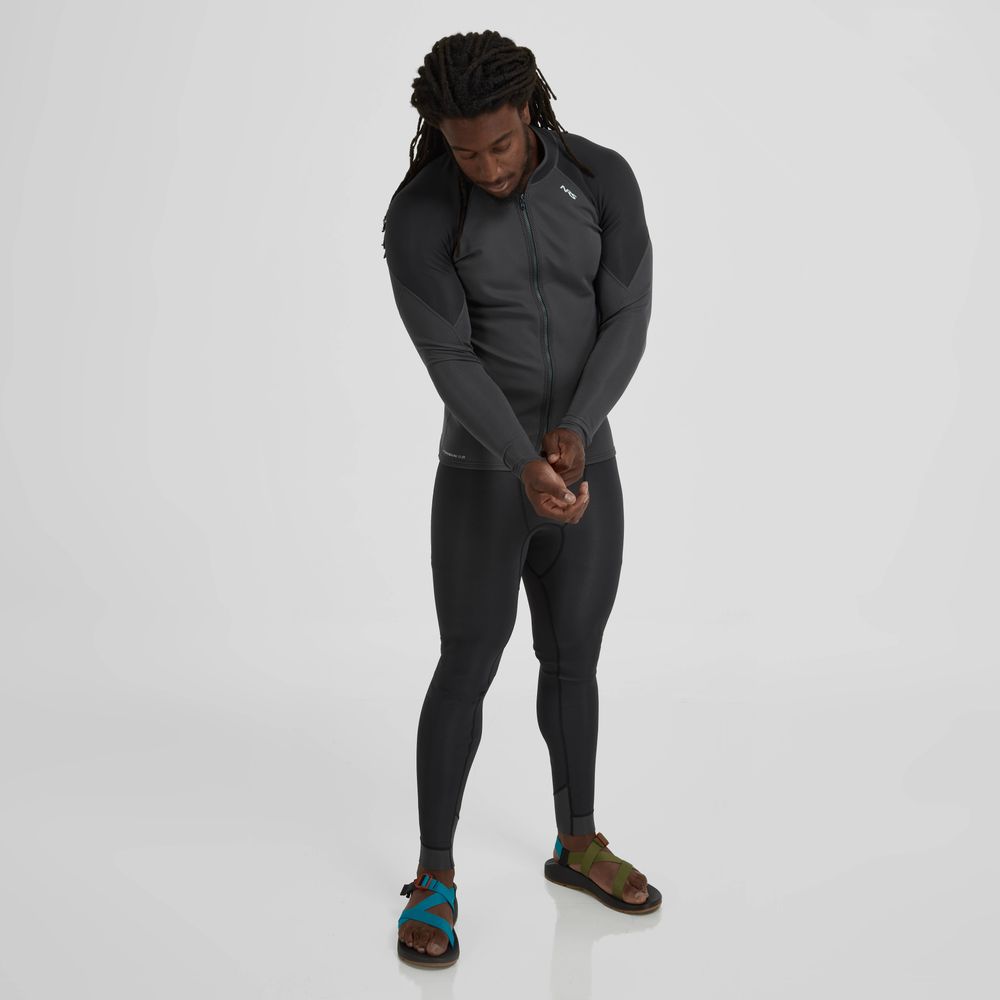 A man in a sleek Hydroskin 0.5mm Jacket by NRS and colorful sandals stands on a plain white background, adjusting his sleeve while looking down.