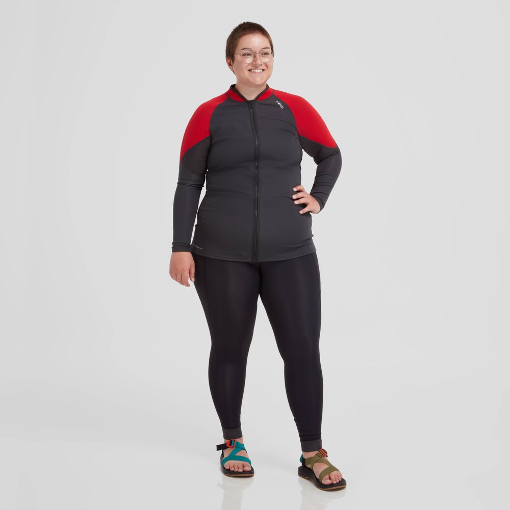 Wearing the NRS Hydroskin 0.5mm Jacket in red and black along with glasses, a person smiles against a plain backdrop, highlighting their paddling skills.