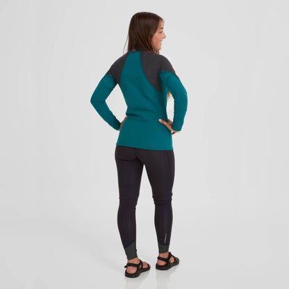 A person stands with hands on hips, wearing a teal and black long-sleeve athletic outfit similar to the NRS Hydroskin 0.5mm Jacket for women, paired with sandals against a plain white background.