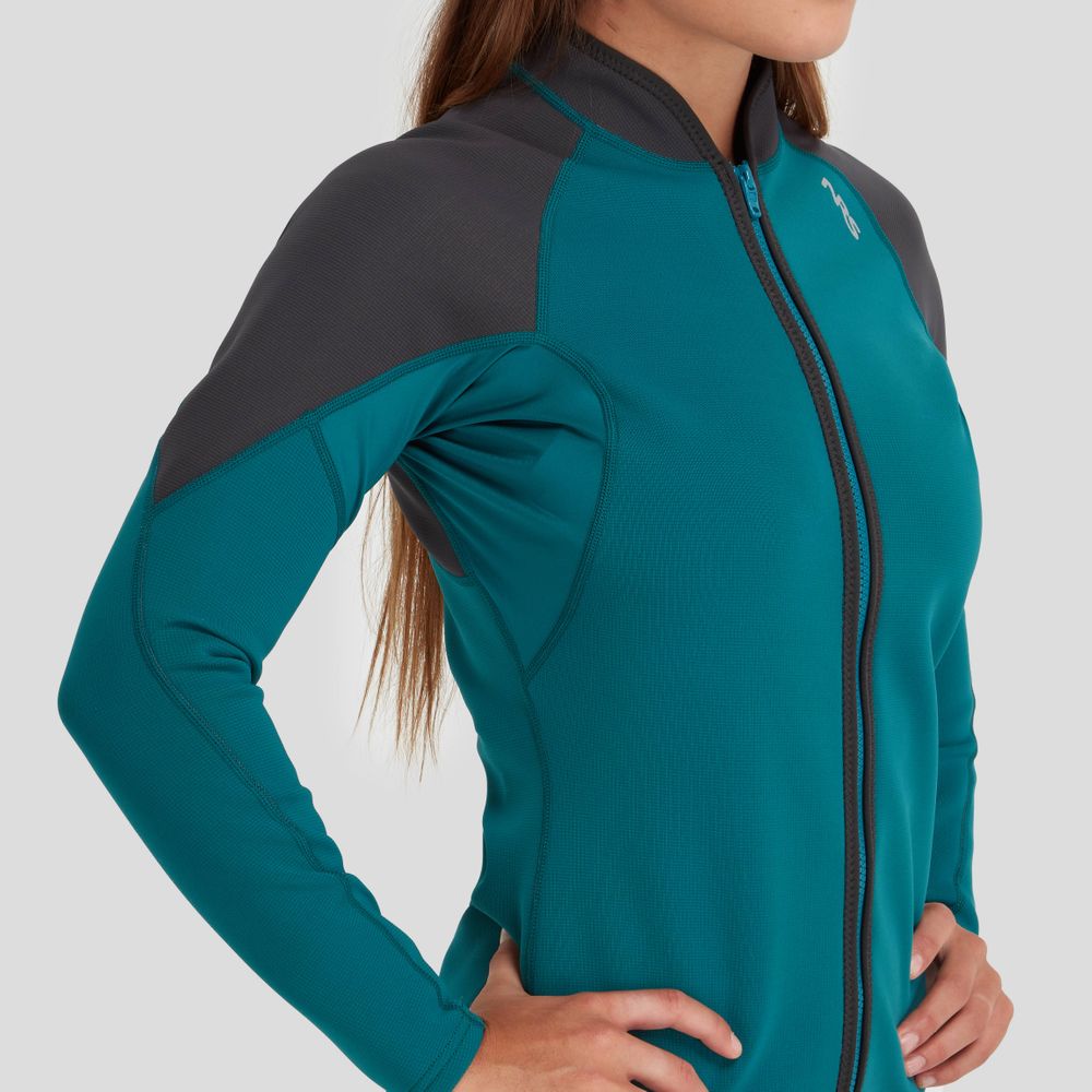 A woman in a teal and gray NRS Hydroskin 0.5mm Jacket stands sideways with hands on hips, poised for peak paddling performance.