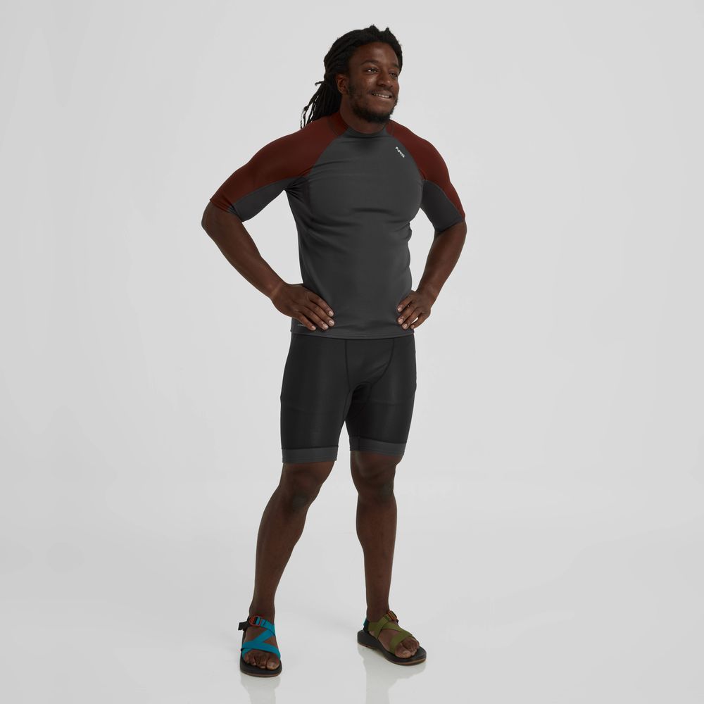 A man is standing in front of a white background, wearing the Hydroskin 0.5 Shorts - Men's from the NRS layering arsenal.