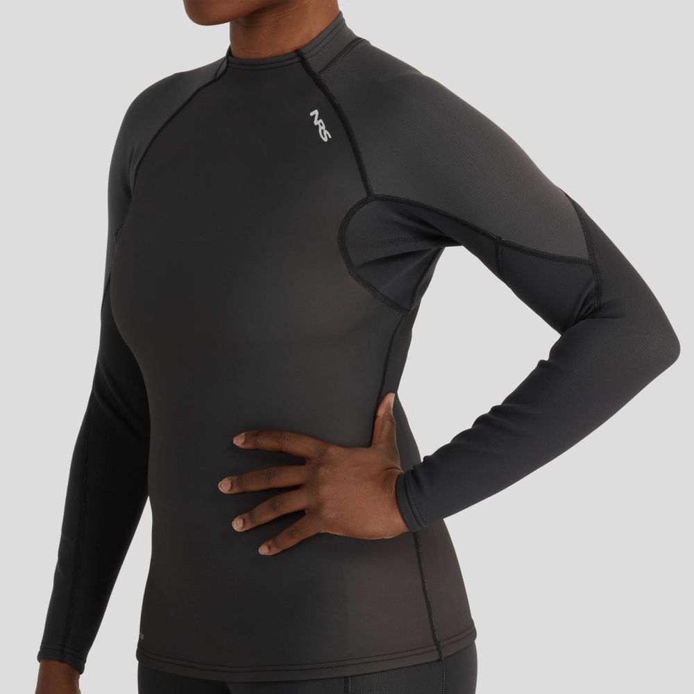 A person wears an NRS Hydroskin 1.0mm Long Sleeve Women's Shirt, featuring a snug wet-suit style fit and neoprene protection, with one hand on their hip against a plain backdrop.