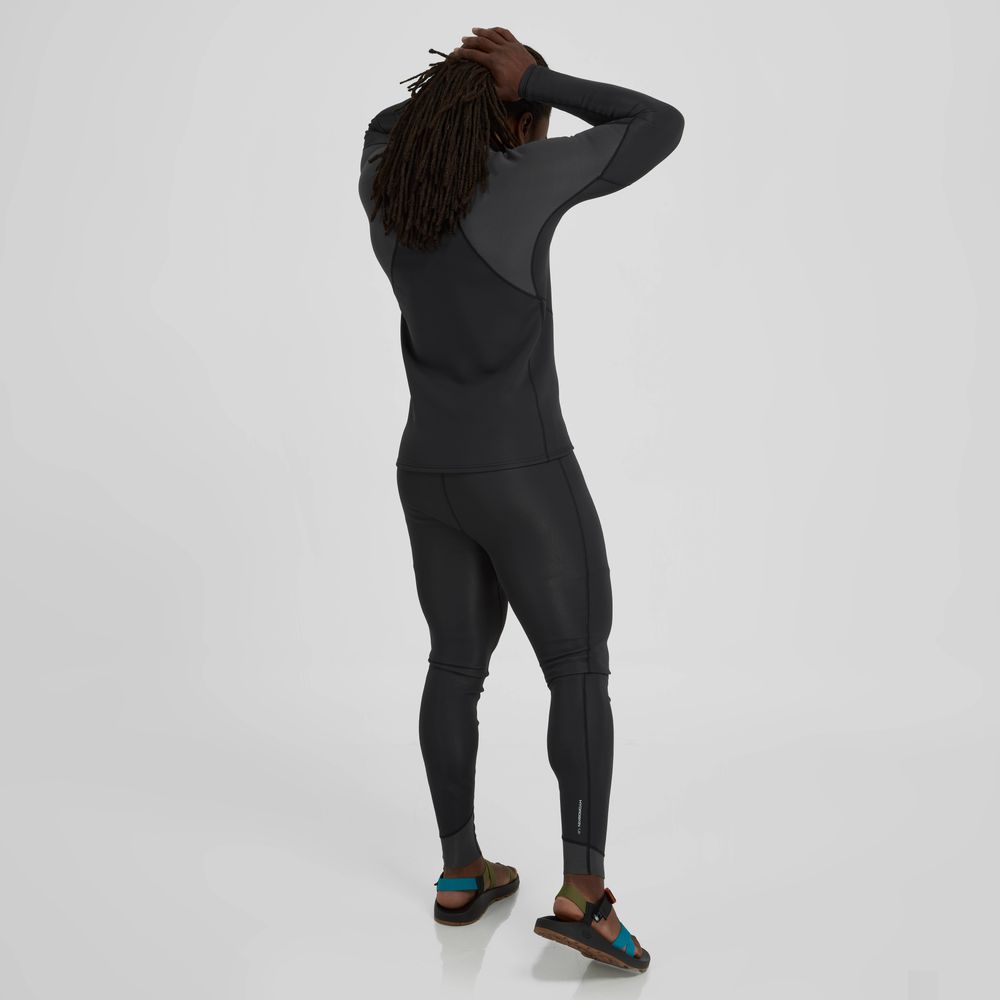 A long-haired person in a dark wetsuit and sandals stands confidently against a light gray background, suggesting superior paddling performance, enhanced by the neoprene insulation of the NRS Hydroskin 1.5mm Jacket for Men.