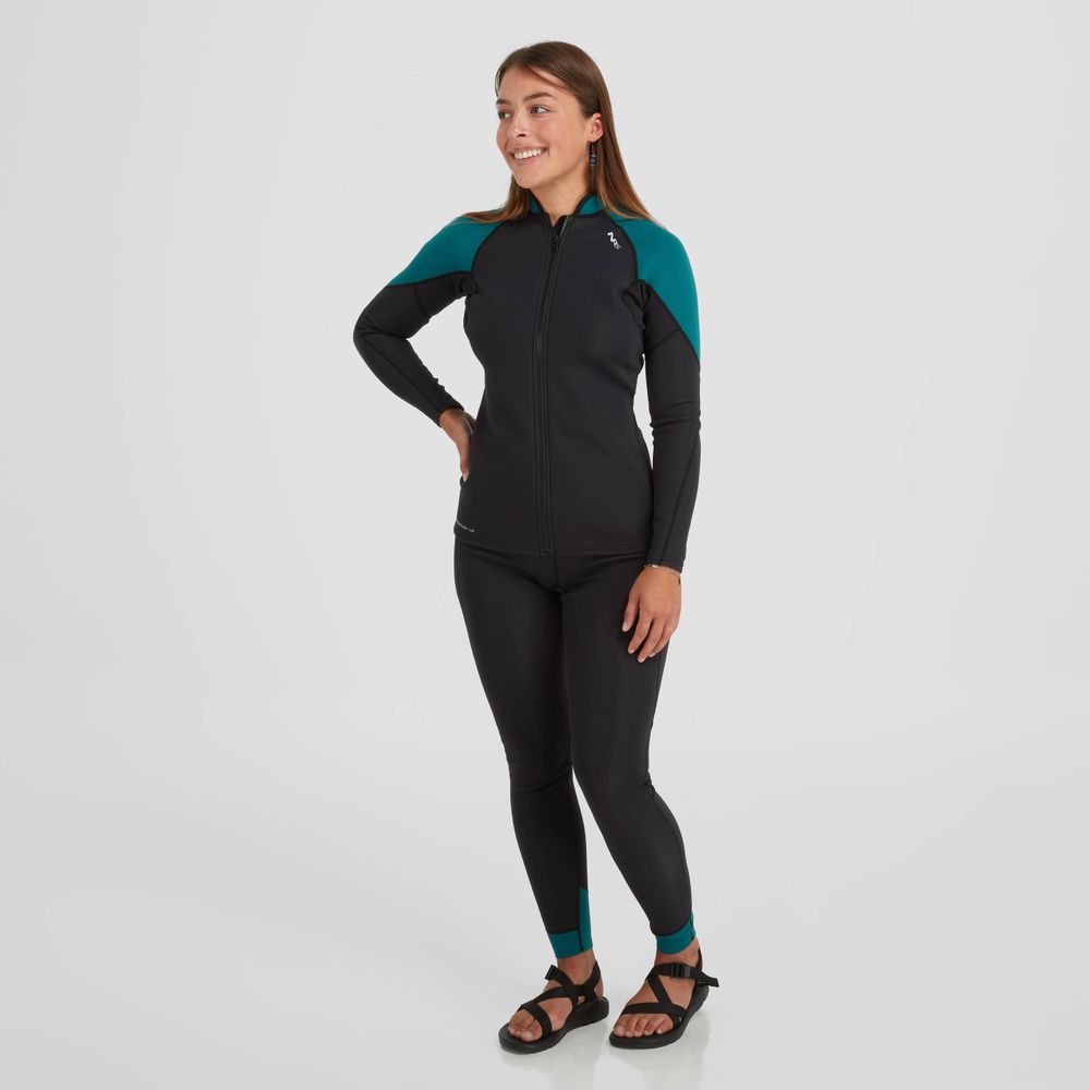 A woman wearing a black and teal wetsuit standing in front of a white background, showcasing the NRS Women's HydroSkin 1.5 Jacket known for its warmth and versatility.