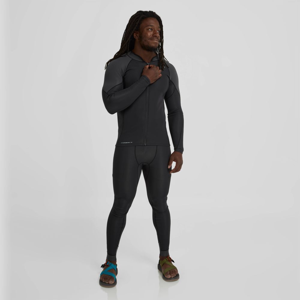 A person in NRS HydroSkin 1.5mm Pants - Men's poses against a plain background, demonstrating excellent paddling performance with warmth and unrestricted movement, accessorized by their sandals.