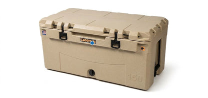 The Canyon Coolers Prospector 150 Raft Cooler is a large tan rotomolded cooler with black latches and handles, a bottom-front drain plug, and Canyon branding—ideal for rugged adventures on the raft.