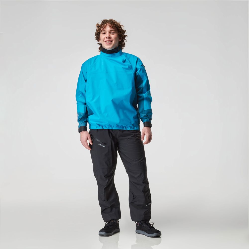 A person wearing the NRS Endurance Splash Jacket - Men's stands against a white background, smiling warmly in dark pants.