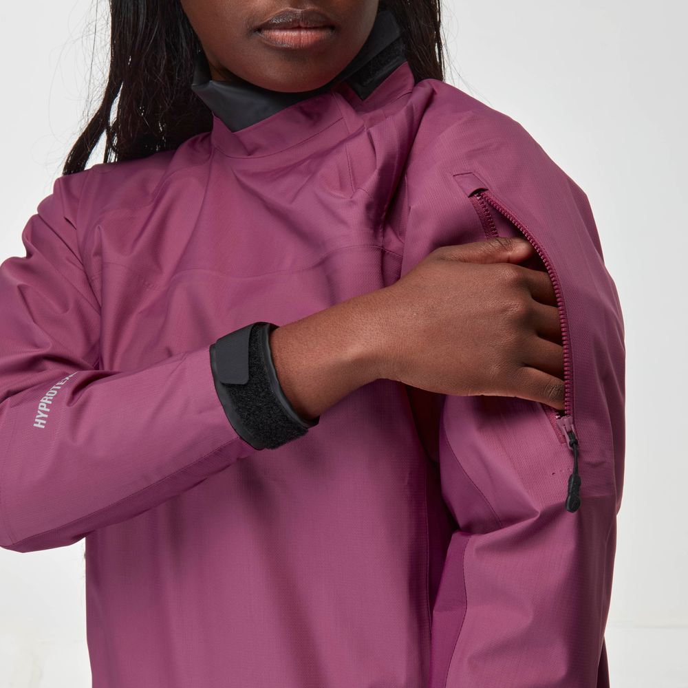 A person wearing a magenta NRS Endurance Splash Jacket - Women's unzips an upper arm pocket on the waterproof jacket.