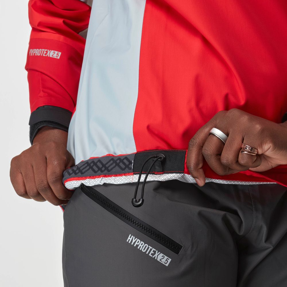 A person adjusts the hem drawcord of a red and gray NRS Endurance Splash Jacket - Women's while wearing matching dark pants, both featuring waterproof protection.