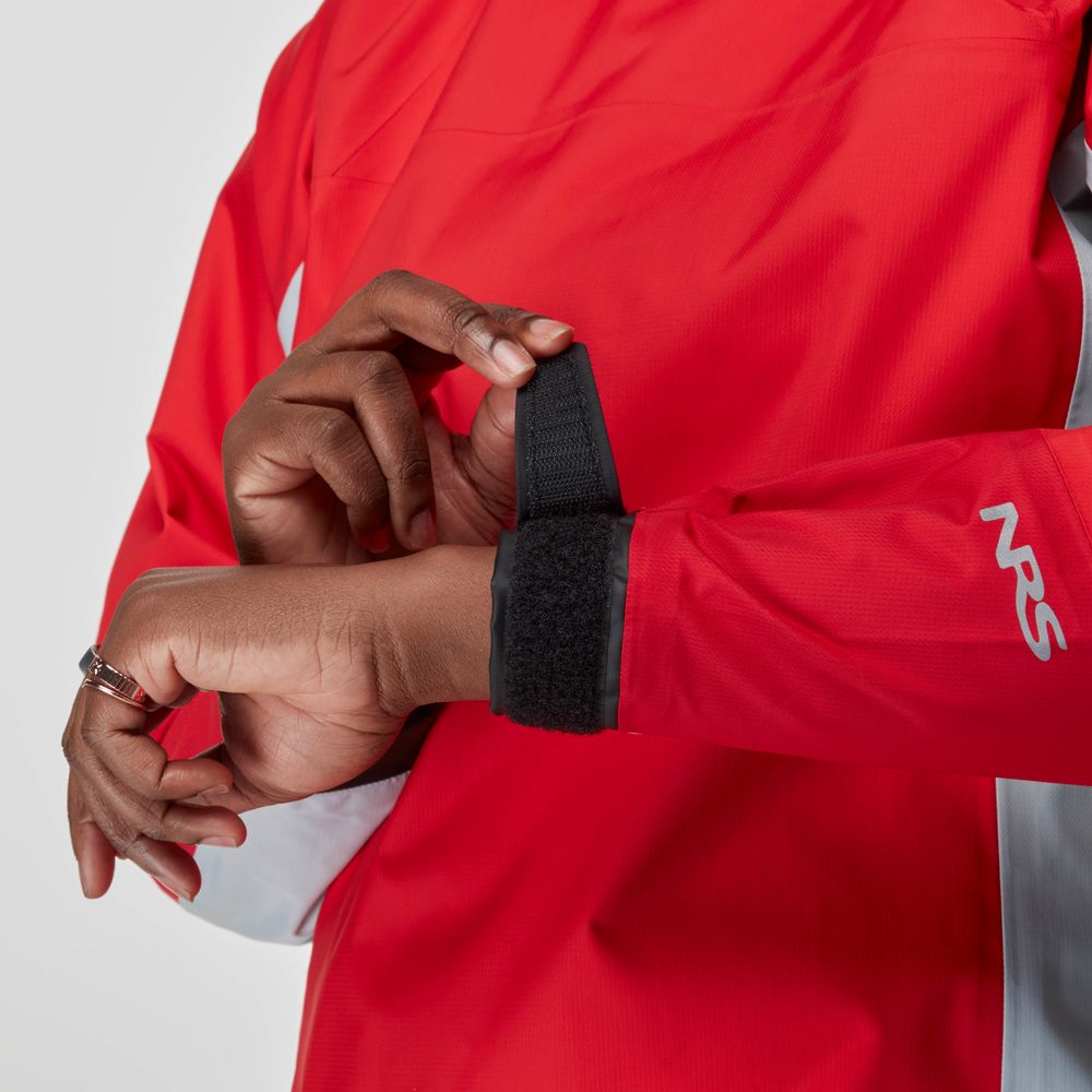 A person adjusts the Velcro wrist strap on the sleeve of an NRS Endurance Splash Jacket - Women's, a red waterproof layer perfect for boating.