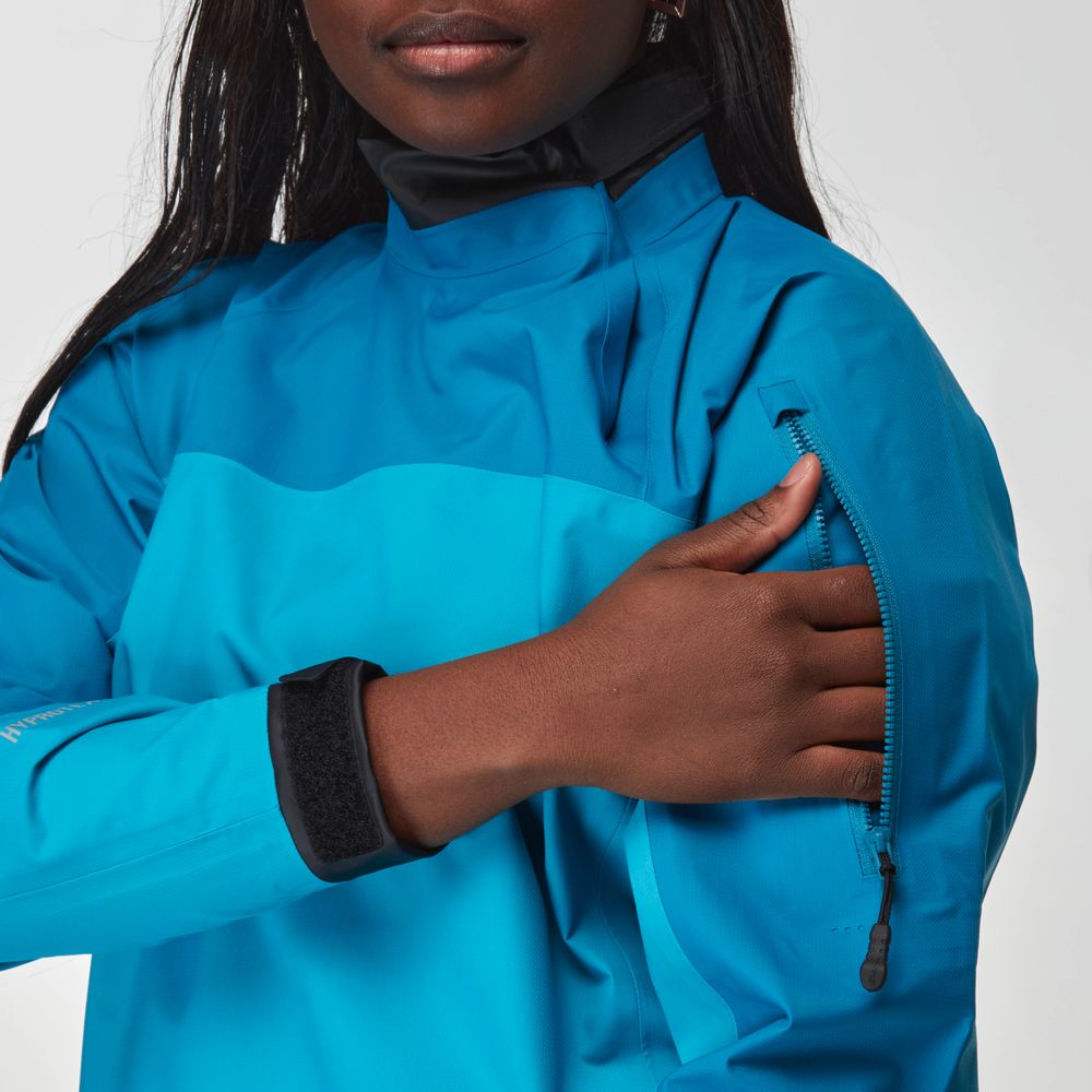 A person wearing the NRS Endurance Splash Jacket - Women's in bright blue unzips a sleeve pocket.